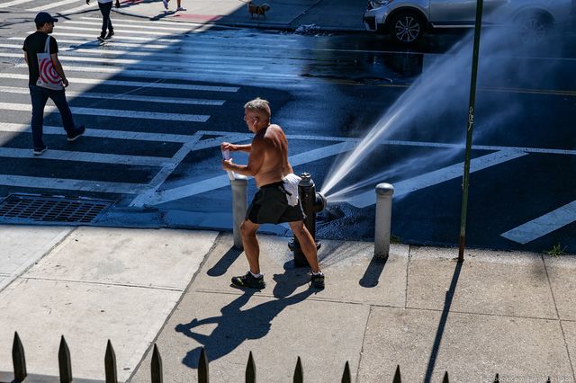 a shirtless man walks past an open hydrant
